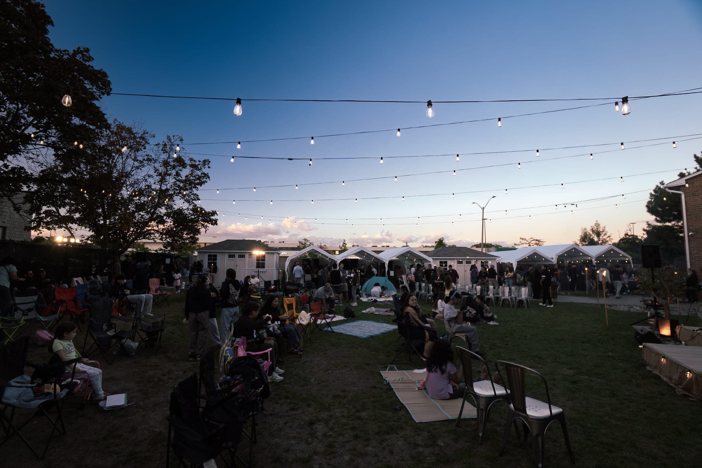 The yard filling up under string lights at dusk