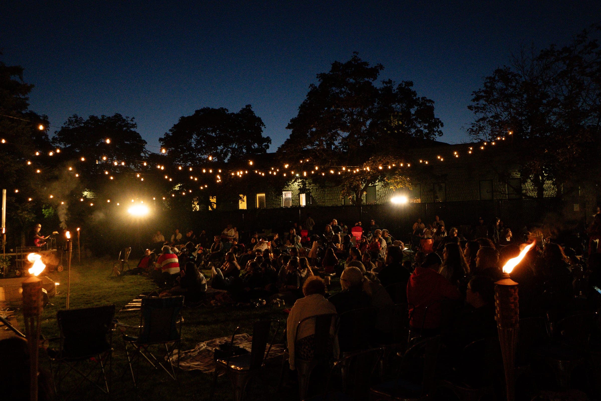 The yard after dark, the whole crowd seated on the grass