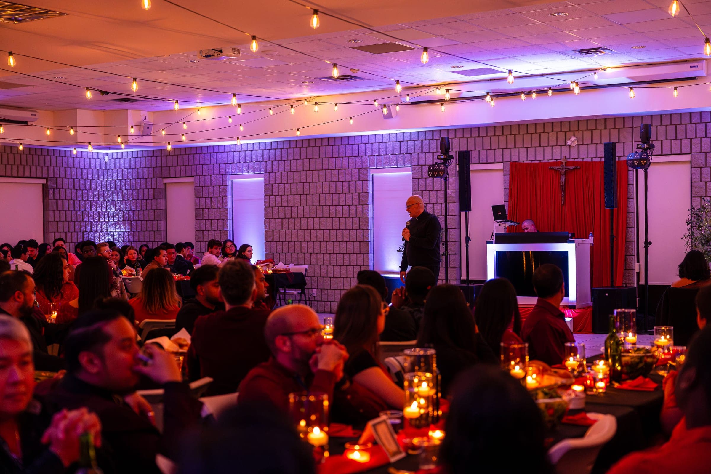 The hall from the back, tables full, the crucifix at the front